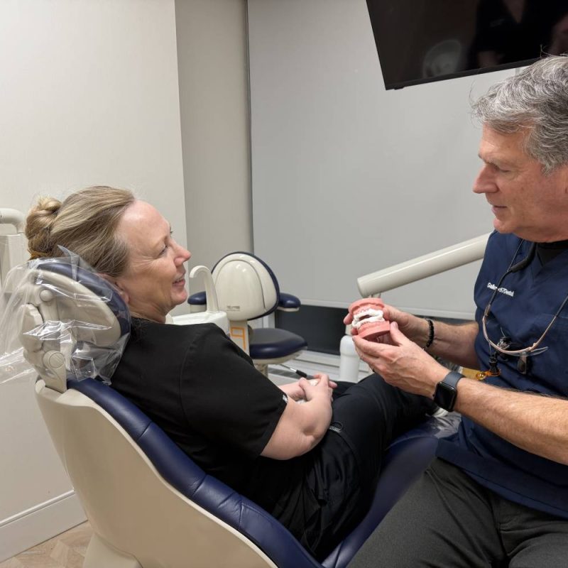 A dentist showing a patient a dental oral appliance used as a natural treatment option for sleep apnea in a dental office – sleep apnea natural treatment midtown nyc