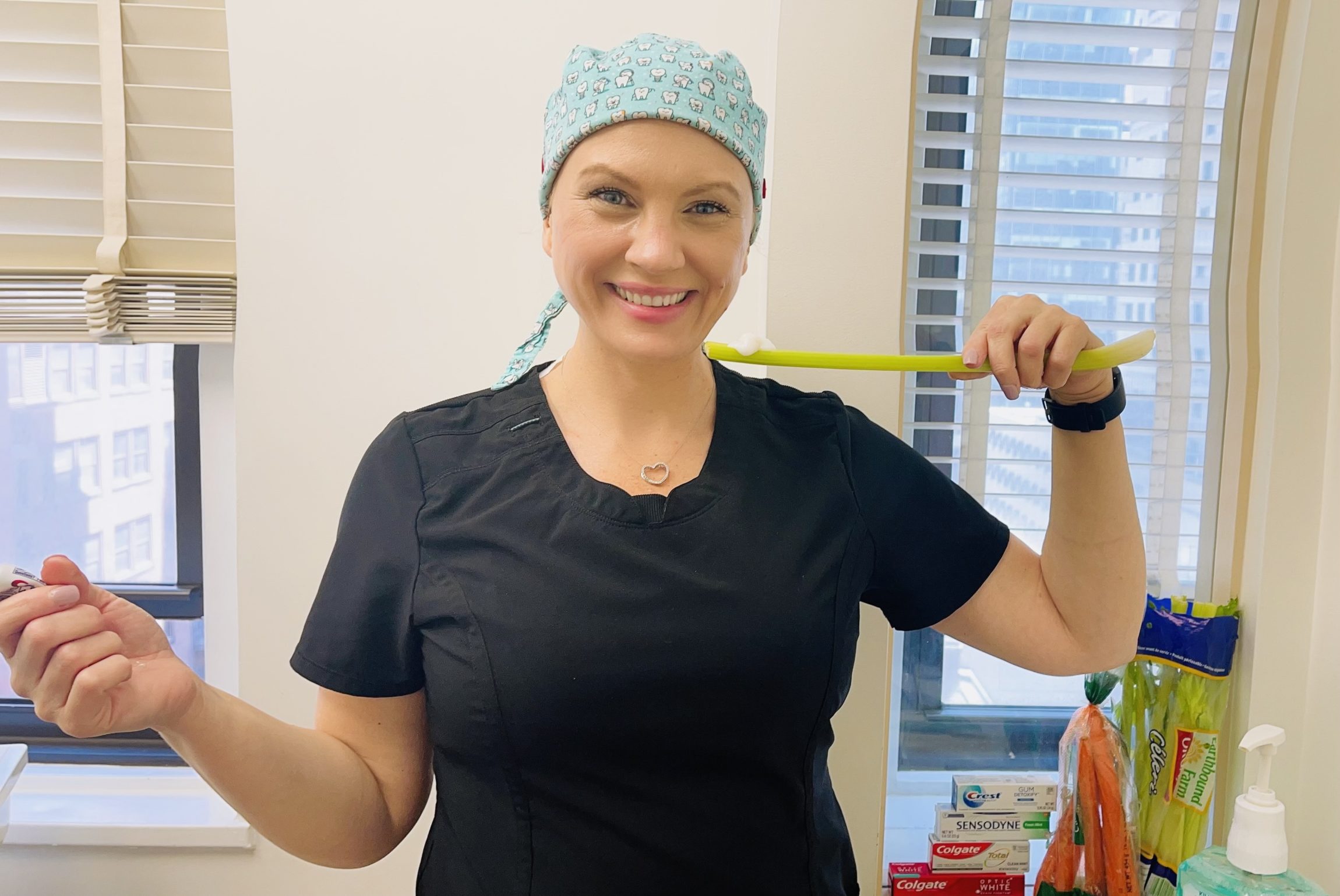 A smiling dental professional holding a long green toothbrush-like tool while standing in a dental office, representing tips on how to brush teeth without toothbrush – how to brush teeth without toothbrush
